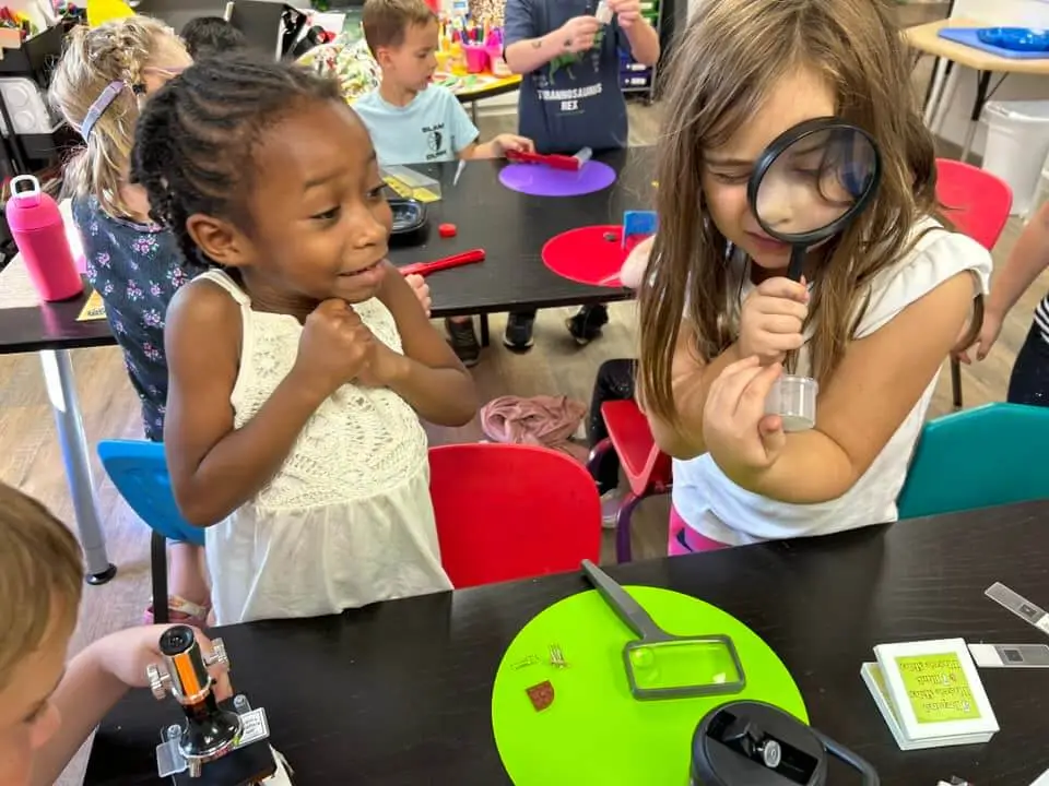 Two Girls Looking At Items Through A Magnifying Glass